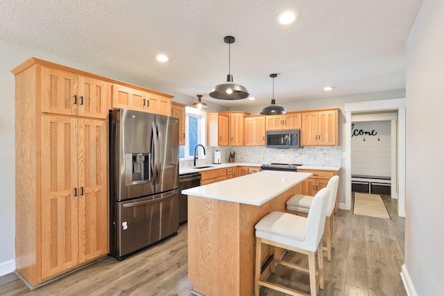 kitchen with a sink, tasteful backsplash, stainless steel appliances, light wood finished floors, and light countertops