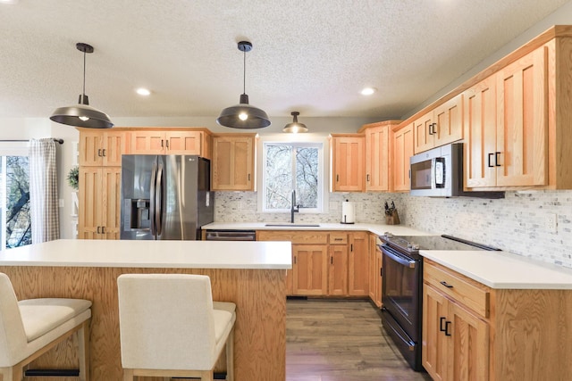 kitchen with a kitchen bar, light brown cabinets, a sink, appliances with stainless steel finishes, and light countertops