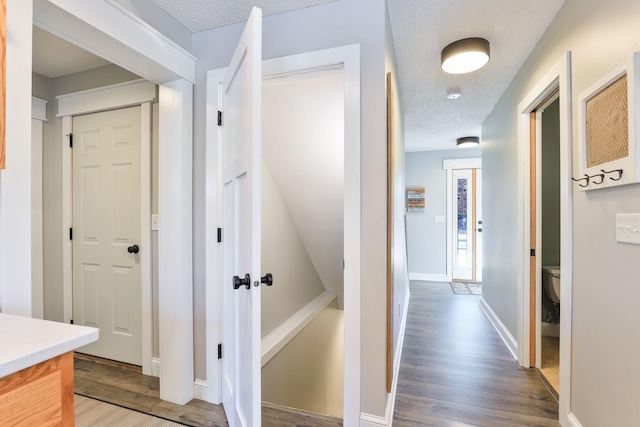 hall featuring wood finished floors, baseboards, and a textured ceiling