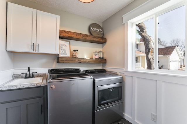 laundry room featuring cabinet space, wainscoting, a sink, a textured ceiling, and independent washer and dryer