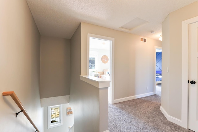 hallway with visible vents, an upstairs landing, a textured ceiling, carpet, and baseboards