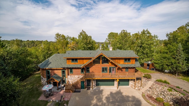 cabin with log siding, stone siding, driveway, and a garage