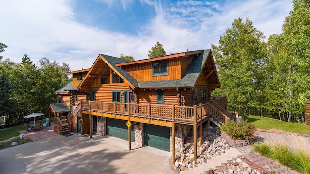 cabin with driveway, roof with shingles, log siding, an attached garage, and stone siding