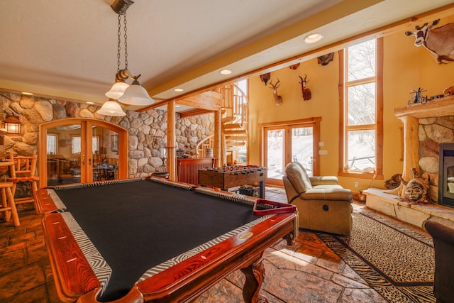 game room with arched walkways, a towering ceiling, stone tile flooring, french doors, and a fireplace