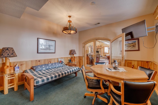 carpeted bedroom with arched walkways, a wainscoted wall, visible vents, wood walls, and a textured ceiling