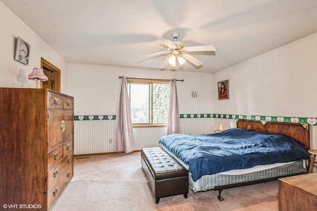 bedroom with a textured ceiling, light carpet, ceiling fan, and wainscoting