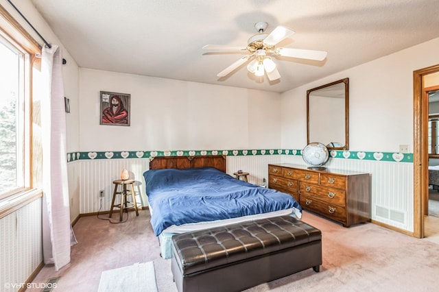 carpeted bedroom with visible vents, ceiling fan, and wainscoting