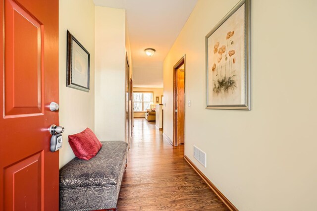 hall with visible vents, baseboards, and wood finished floors