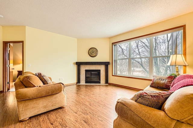 living room with a tile fireplace, a textured ceiling, baseboards, and wood finished floors