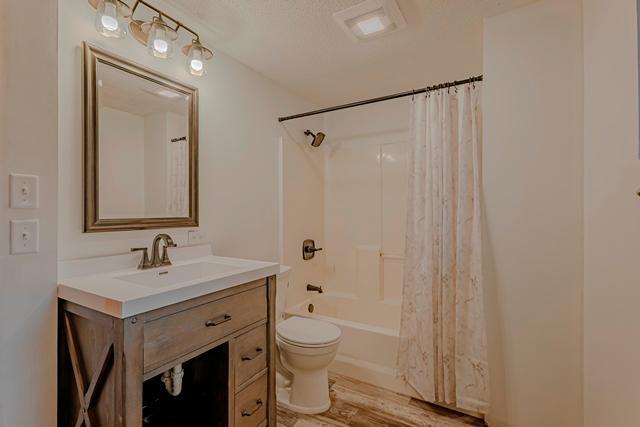 bathroom with shower / bathtub combination with curtain, toilet, wood finished floors, and vanity