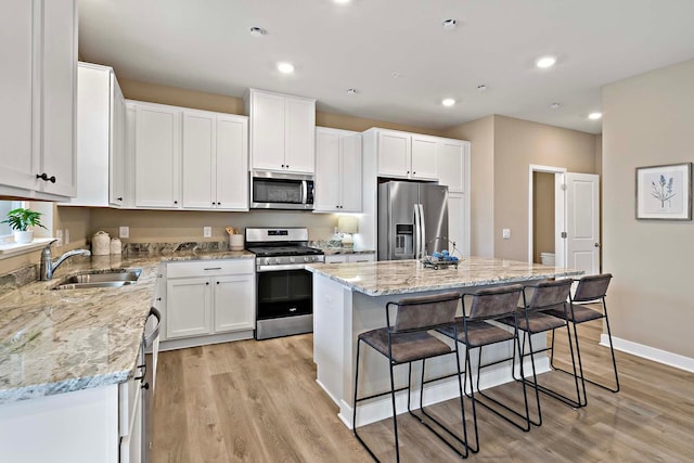 kitchen featuring light wood finished floors, a kitchen bar, stainless steel appliances, white cabinetry, and a sink