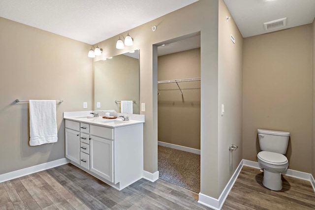 bathroom featuring a sink, toilet, visible vents, wood finished floors, and a walk in closet