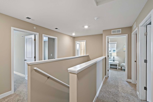 hallway with light carpet, visible vents, and an upstairs landing