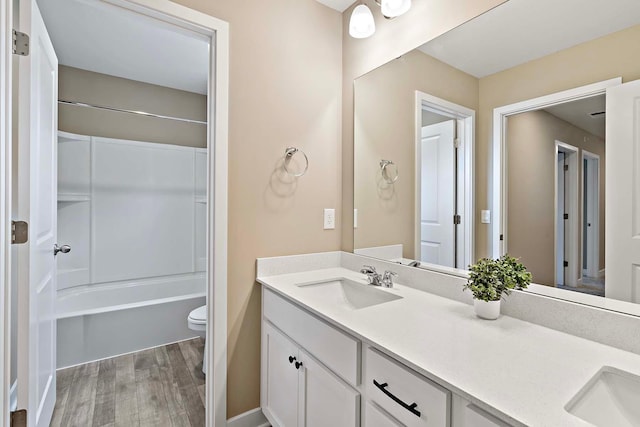 full bath featuring wood finished floors, a sink, tub / shower combination, double vanity, and toilet