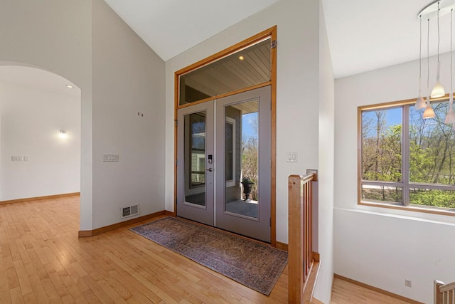 foyer entrance featuring arched walkways, light wood-style flooring, baseboards, and vaulted ceiling