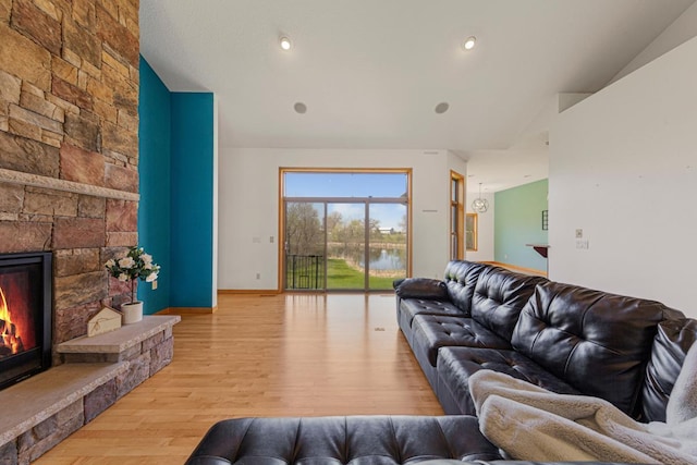 living area featuring a stone fireplace, wood finished floors, a water view, and baseboards