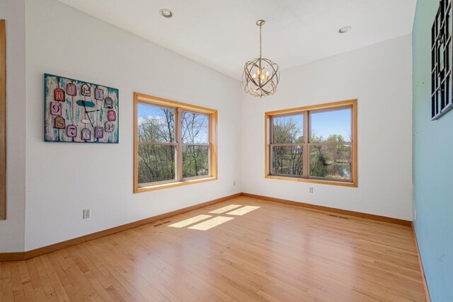spare room with a chandelier, plenty of natural light, wood finished floors, baseboards, and recessed lighting
