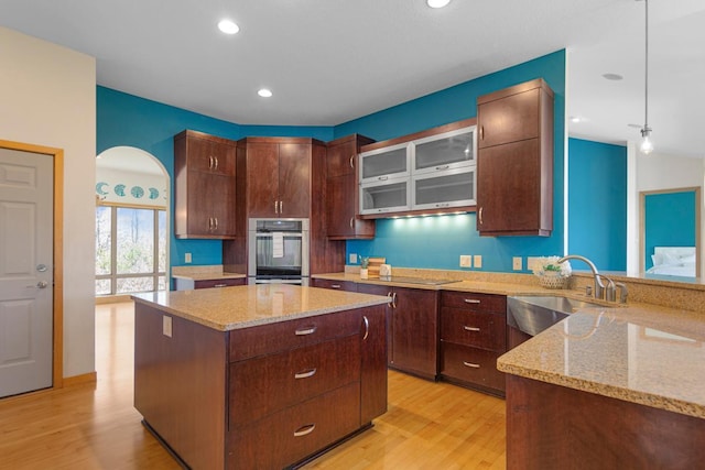 kitchen featuring a sink, double oven, light wood-style flooring, light stone counters, and a center island
