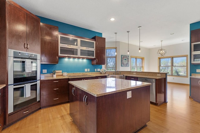 kitchen featuring stainless steel appliances, light wood-style floors, a center island, a peninsula, and glass insert cabinets