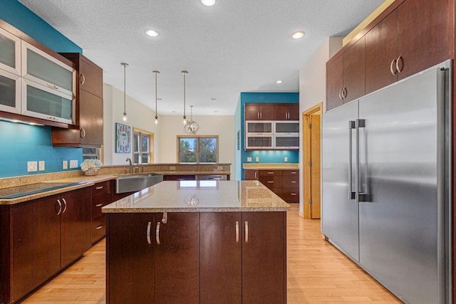 kitchen featuring built in fridge, a sink, black electric stovetop, light wood-type flooring, and glass insert cabinets
