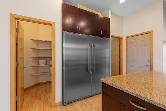 kitchen featuring built in fridge, light wood-style floors, dark brown cabinets, recessed lighting, and light stone counters