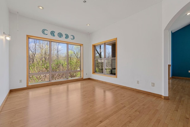 unfurnished room featuring wood finished floors, baseboards, recessed lighting, and arched walkways
