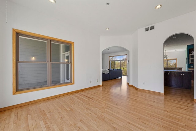 spare room featuring light wood finished floors, recessed lighting, arched walkways, and baseboards