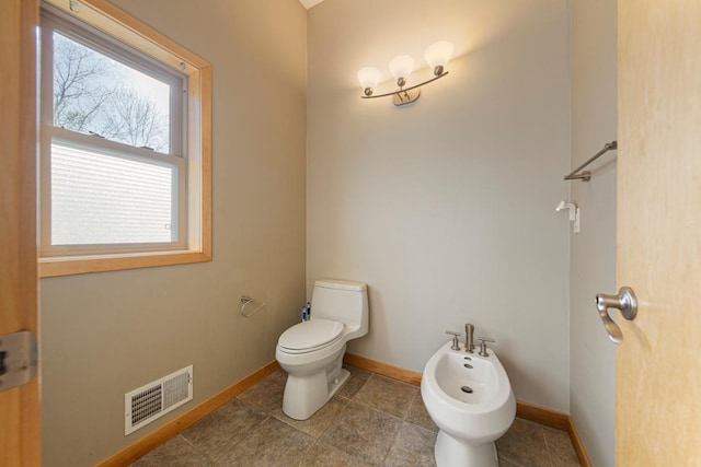half bathroom featuring a bidet, baseboards, toilet, and tile patterned floors