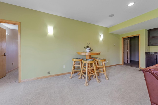 dining room featuring light carpet, baseboards, and bar area