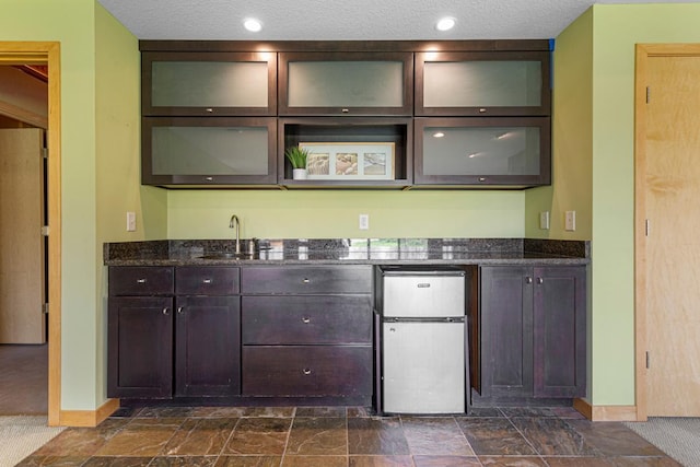 indoor wet bar with baseboards, refrigerator, and dark stone finish flooring