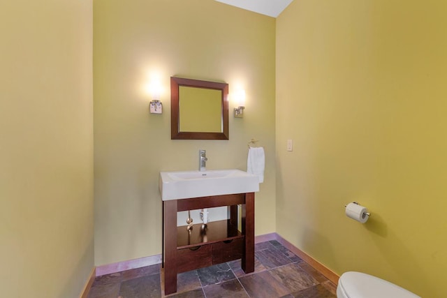 bathroom with baseboards, toilet, stone finish floors, and vanity