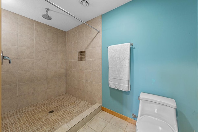 full bath featuring tile patterned floors, a tile shower, toilet, and baseboards