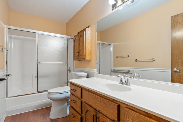 bathroom featuring enclosed tub / shower combo, toilet, a wainscoted wall, wood finished floors, and vanity