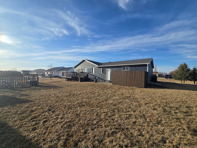 back of property with a deck, fence, and a lawn