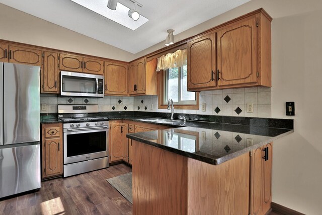 kitchen with vaulted ceiling, brown cabinets, a peninsula, stainless steel appliances, and a sink