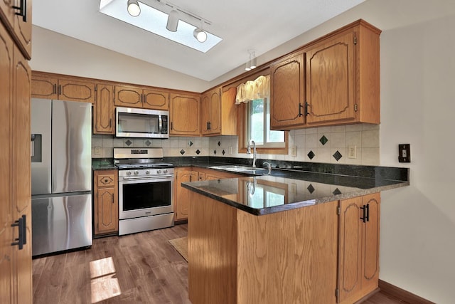 kitchen with brown cabinets, a sink, stainless steel appliances, a peninsula, and vaulted ceiling