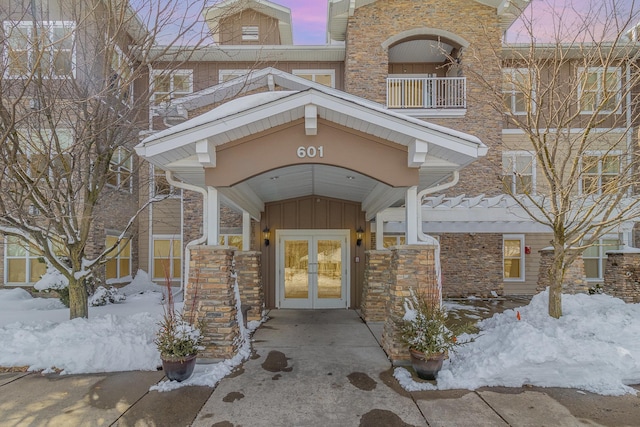 snow covered property entrance featuring brick siding, board and batten siding, and french doors