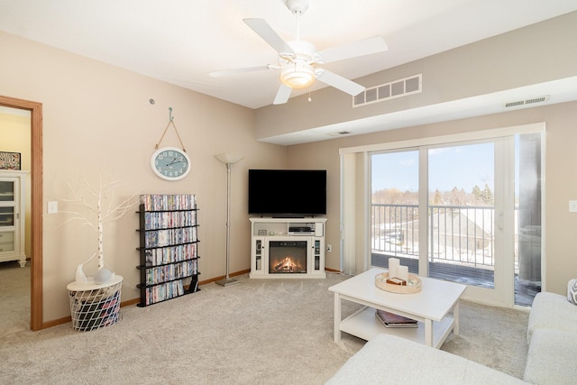 living room with a warm lit fireplace, ceiling fan, visible vents, and carpet flooring