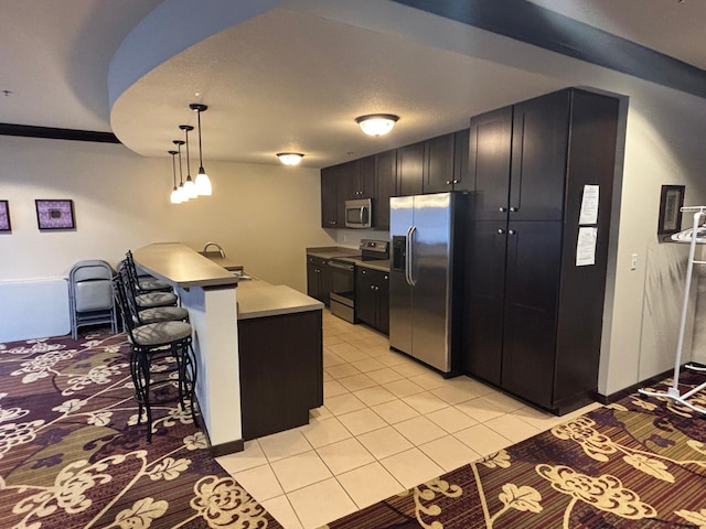 kitchen with a breakfast bar area, stainless steel appliances, light tile patterned flooring, a sink, and a peninsula