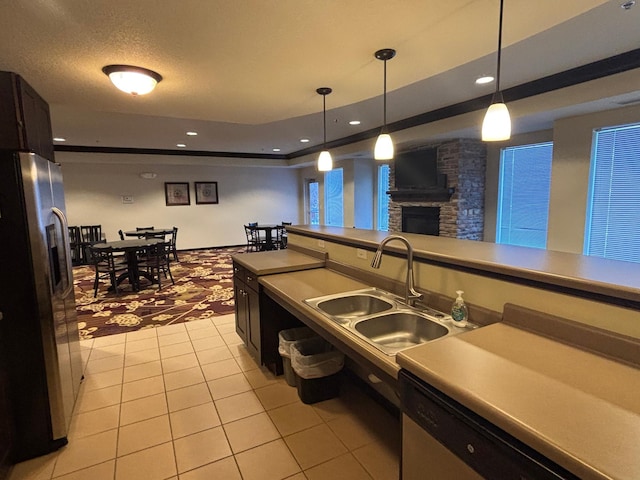 kitchen featuring decorative light fixtures, light tile patterned floors, appliances with stainless steel finishes, a sink, and a stone fireplace