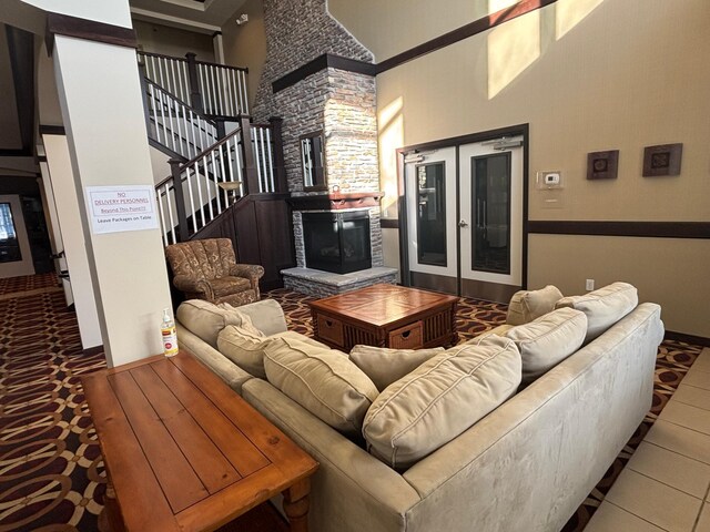 living area with a towering ceiling, stairs, and a stone fireplace