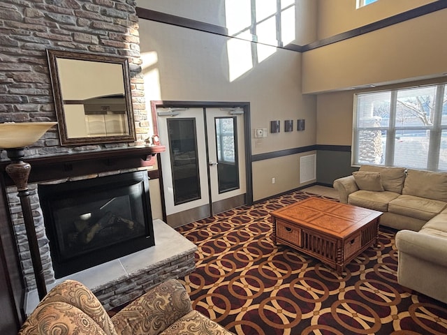 living area with a high ceiling, visible vents, a wealth of natural light, and a glass covered fireplace