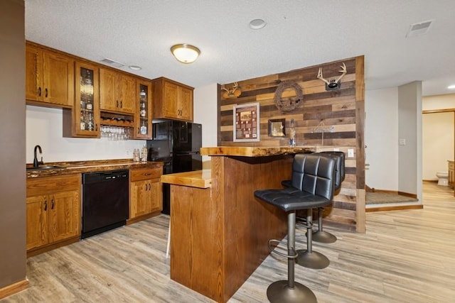 kitchen with light wood finished floors, a sink, black appliances, a kitchen breakfast bar, and brown cabinets