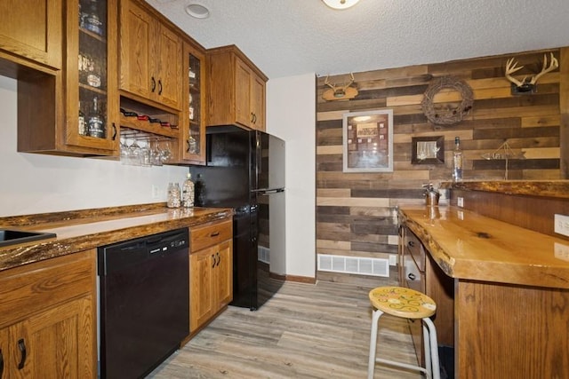 kitchen featuring visible vents, black appliances, a textured ceiling, wooden walls, and light wood finished floors