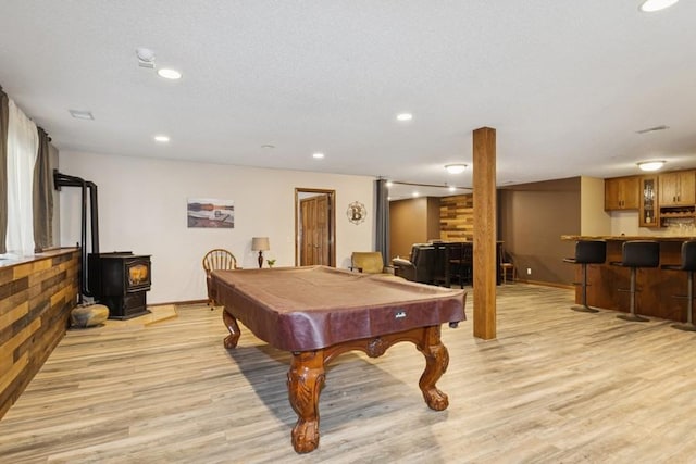 rec room featuring bar area, recessed lighting, light wood finished floors, baseboards, and a wood stove