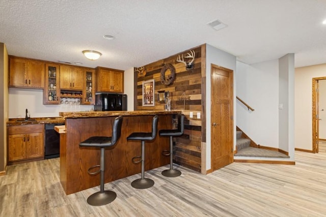 bar featuring light wood finished floors, visible vents, stairway, wet bar, and black appliances