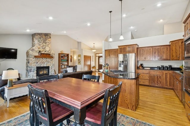 dining space with a stone fireplace, light wood-style floors, and high vaulted ceiling