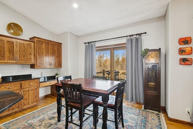 dining space featuring baseboards, lofted ceiling, and light wood finished floors