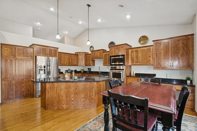 kitchen featuring light wood-style floors, appliances with stainless steel finishes, dark countertops, brown cabinets, and a center island