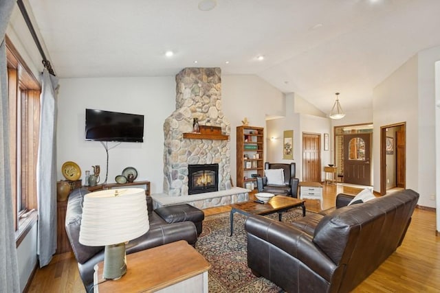 living room with lofted ceiling, a stone fireplace, and wood finished floors